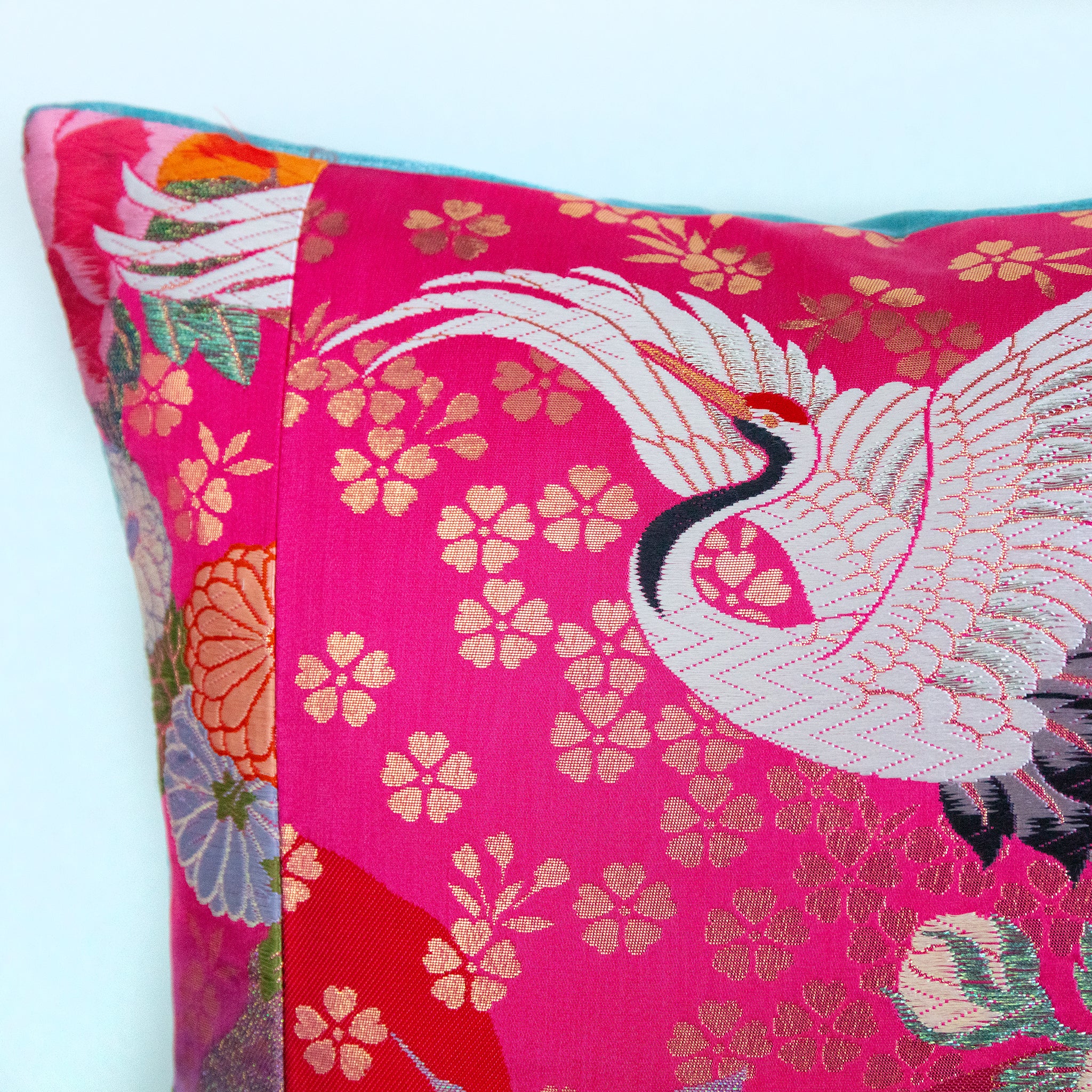 Close-up of the embroidered pink crane and teal velvet edge highlighting intricate needlework detail on the cushion.
