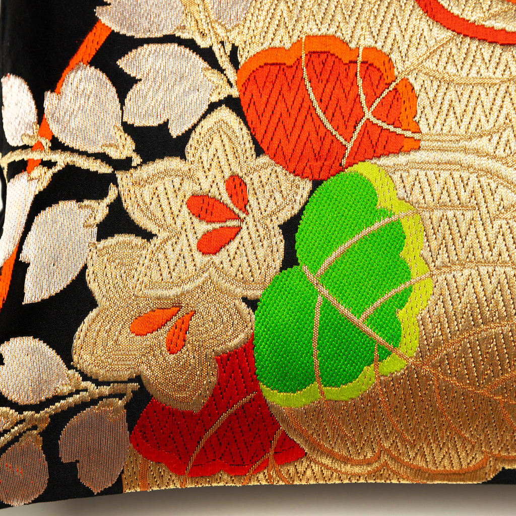 Close up detail of kiri paulownia motif in gold thread with red and green accents on a Japanese obi