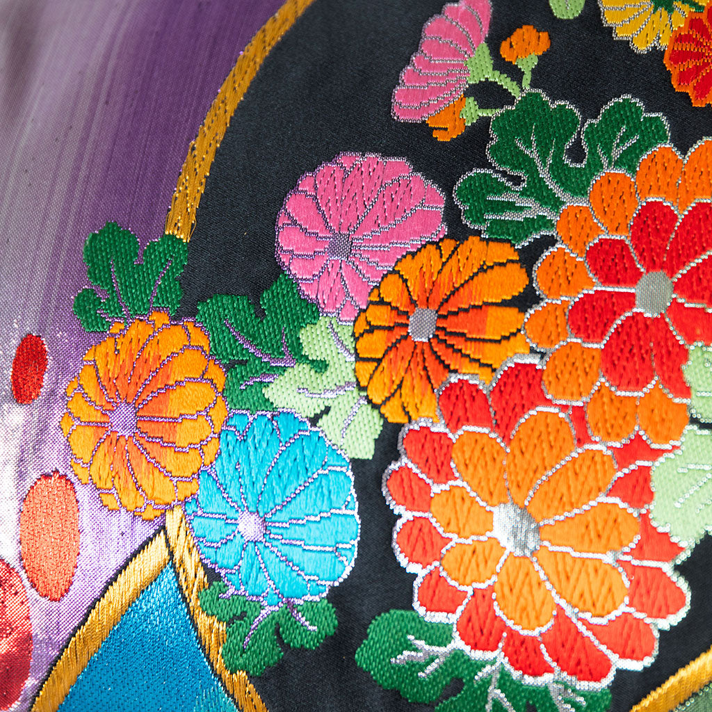 Close-up of the embroidered rainbow silk accents on grey velvet bolster cushion edge, highlighting intricate stitching and