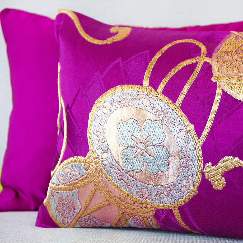 Detail of a woven silk gold Japanese drum on a purple silk cushion with the edge of a second purple silk cushion showing behind it.