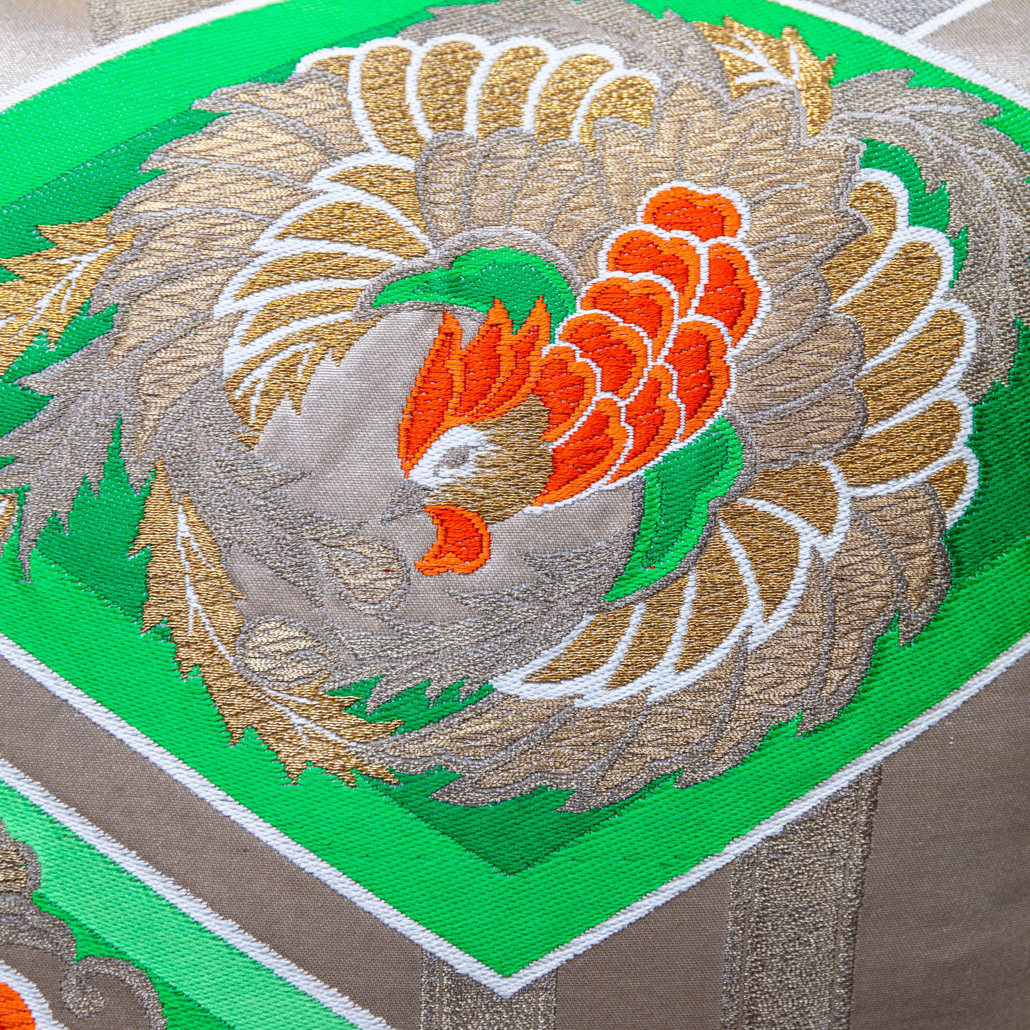 Close-up of the golden phoenix embroidered detailing on the green silk obi cushion's front surface, highlighting intricate