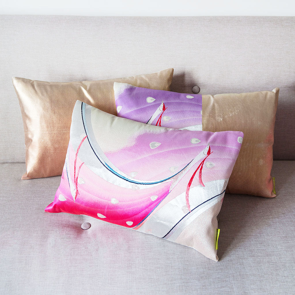 Collection of cushions cut from a vintage Japanese silk obi, pink peacock cushion in front of two gold cushions on neutral sofa.