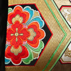 Detail of a woven gold obi with hexagon pattern and red flower motif.