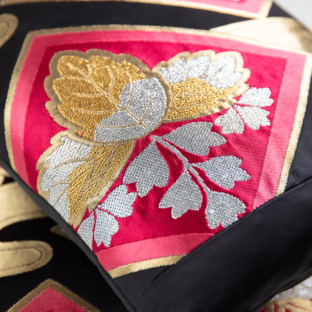 Close up of vintage obi silk pillow in black with pink, gold and silver floral motifs and black silk border.