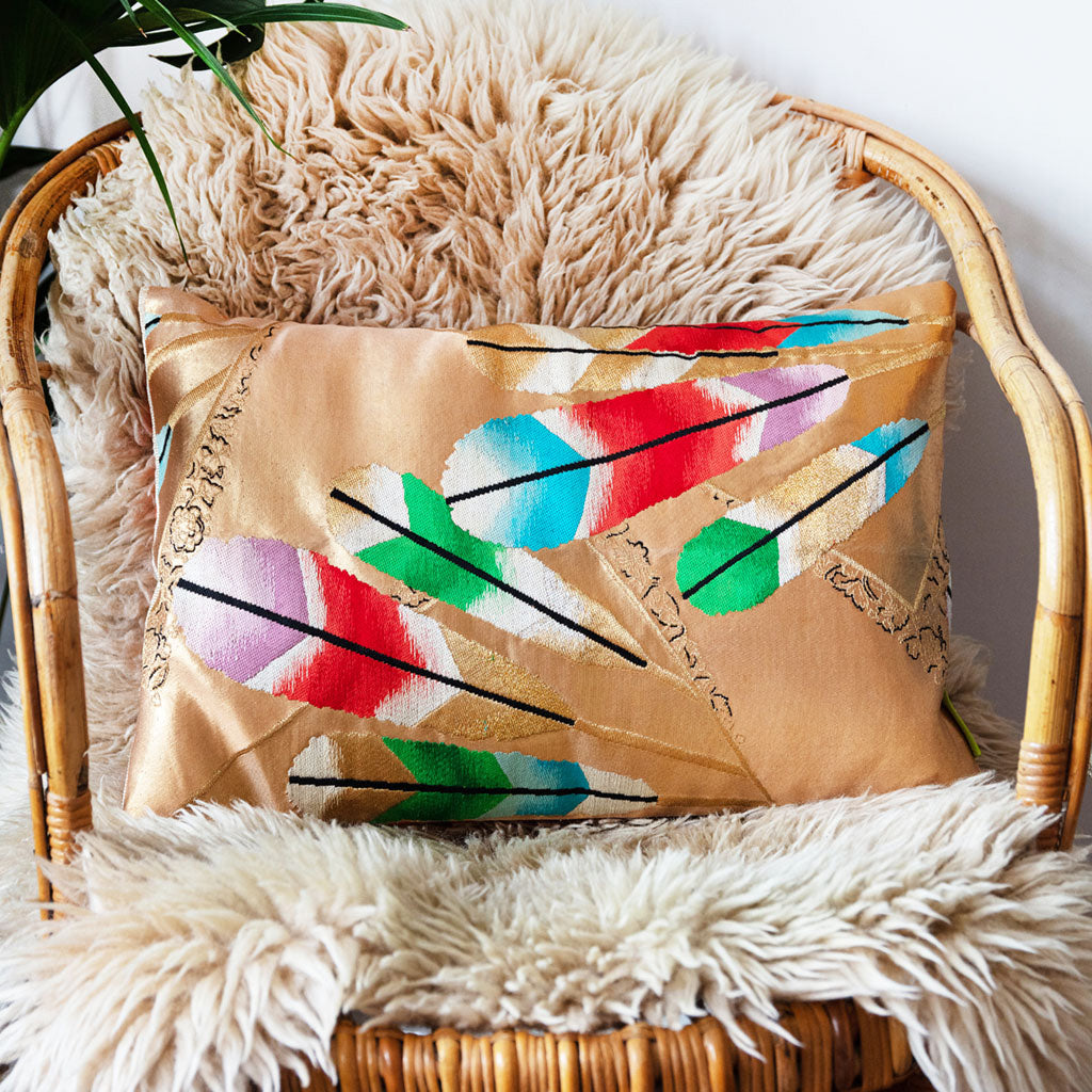 Gold Japanese obi cushion with feather design on a cane chair.