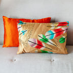 Gold obi cushion with feather motifs in front of an orange silk cushion (the colour of the reverse of the cushion) on a neutral sofa.