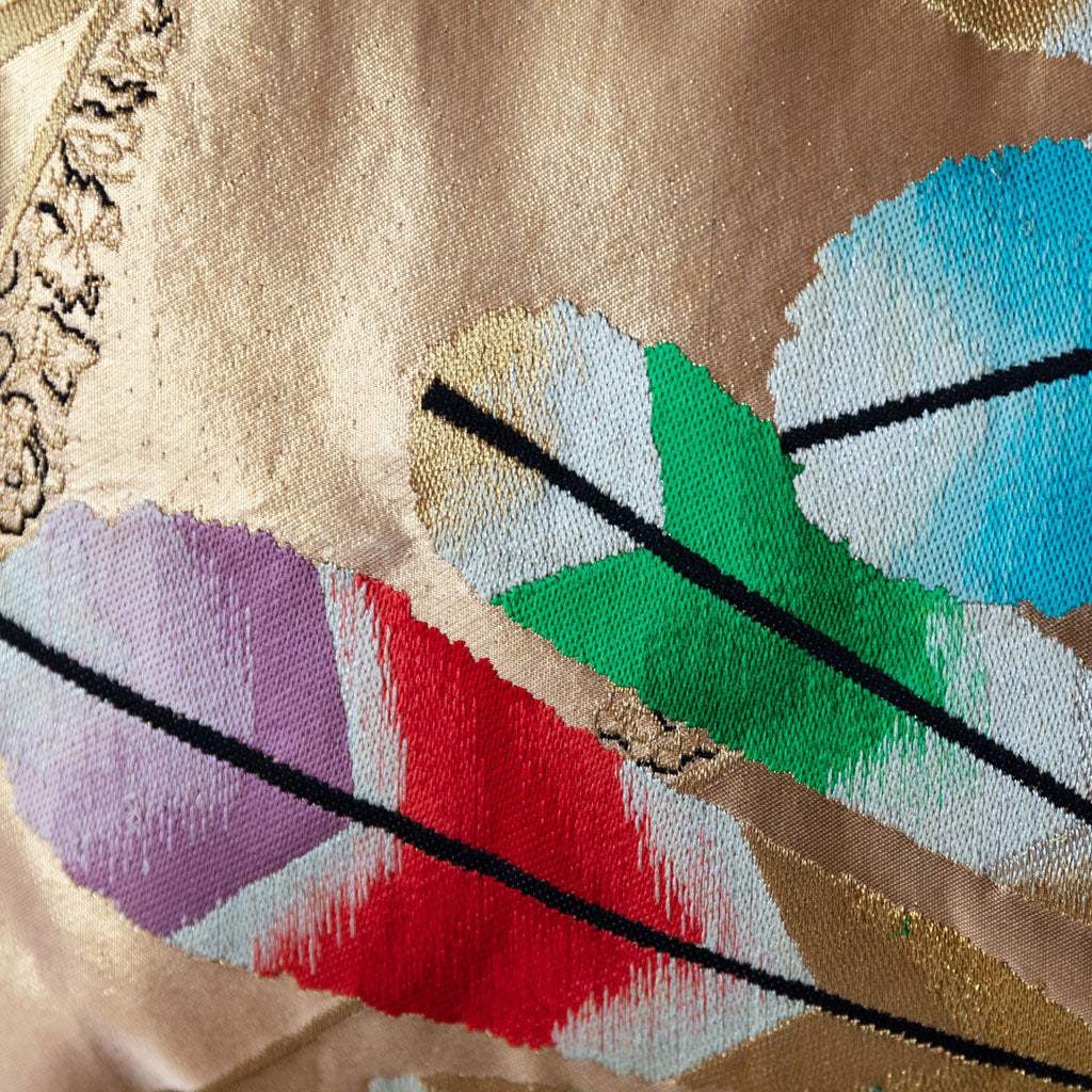 Close up of colourful feather motif on a gold obi silk cushion.
