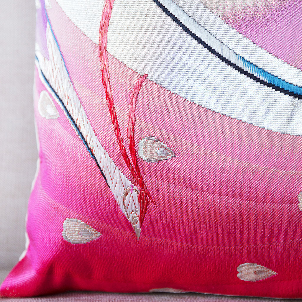 Close-up of silver peacock feather embroidery detail on the pink silk obi cushion’s corner.