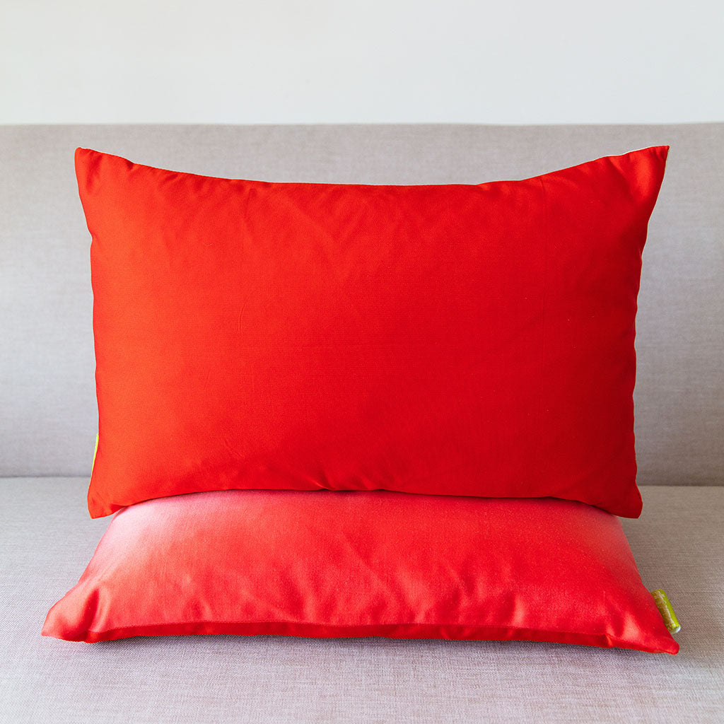 Red rectangular silk cushion stacked on an ombre red cushion on a neutral sofa.