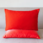 Red rectangular silk cushion stacked on an ombre red cushion on a neutral sofa.