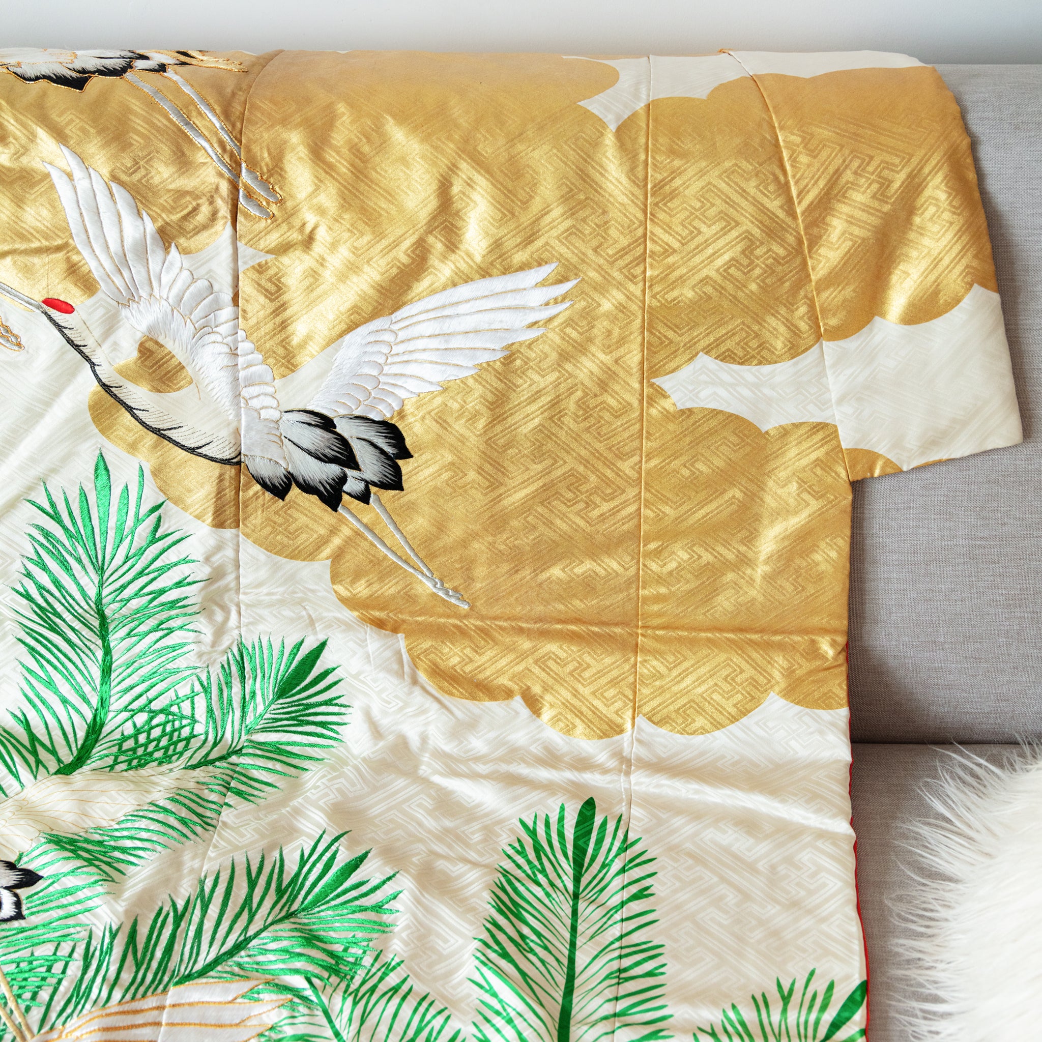 close up of silk throw made from vintage kimono silk in cream, showing collar detail, gold clouds pattern and flying crane, on sofa.