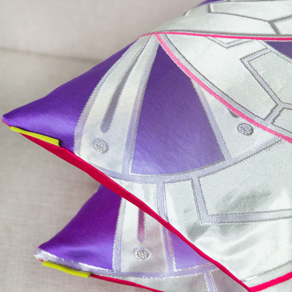 Side view of the corner of two of the pillows showing the purple and silver fronts and bright pink backs.
