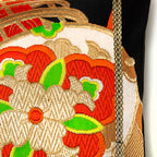 Close up detail of a woven silk Japanese obi with drum pattern and red and green accents