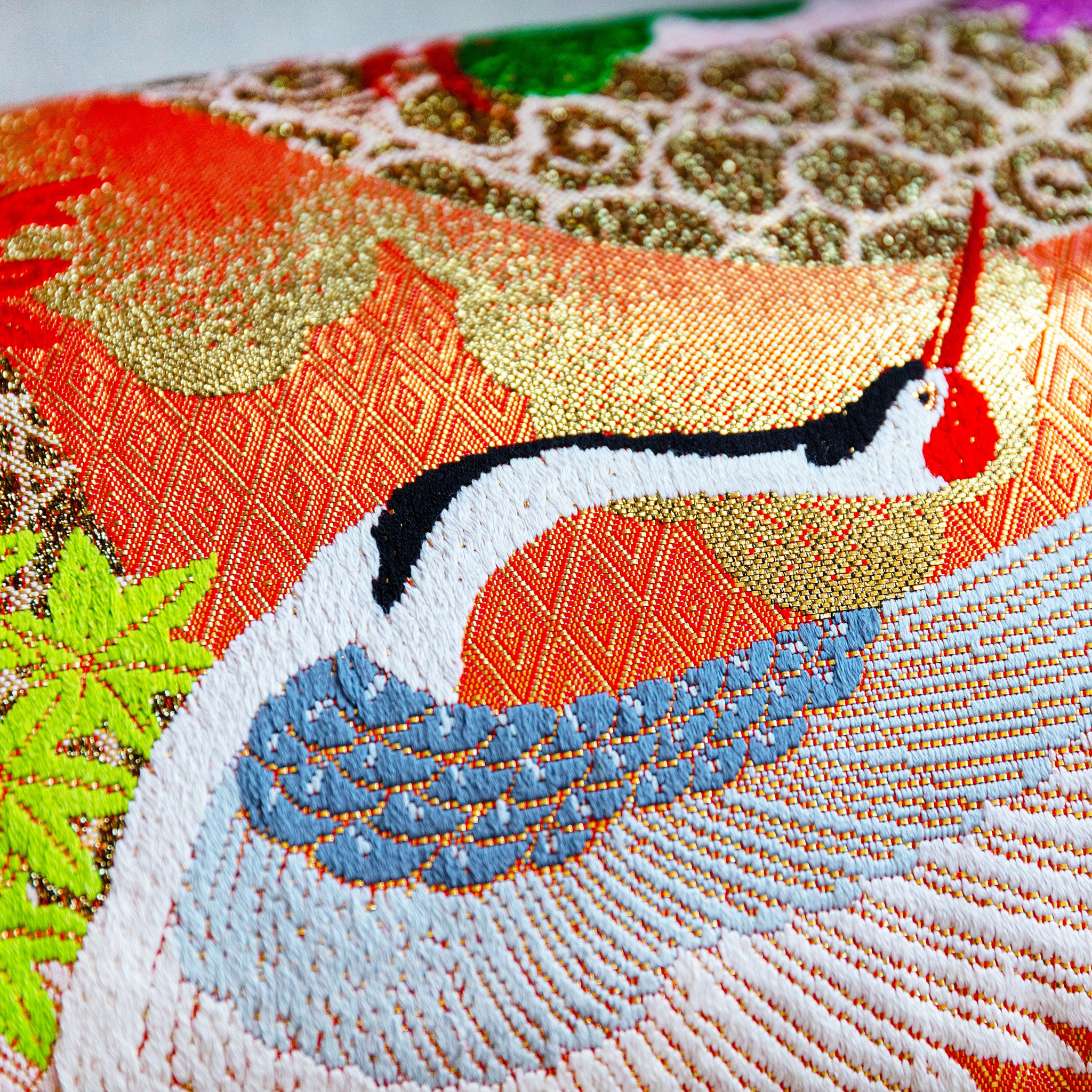 Close-up of vibrant kimono silk cranes embroidered onto lush blue velvet fabric, highlighting intricate stitching and