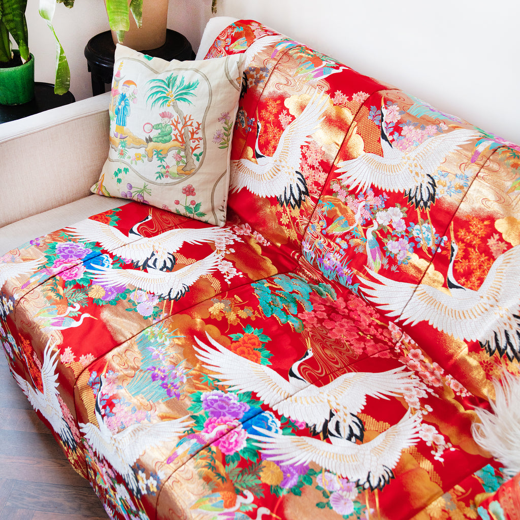 silk throw made from vintage kimono silk on a sofa. Red base, colourful flowers and white embroidered cranes.