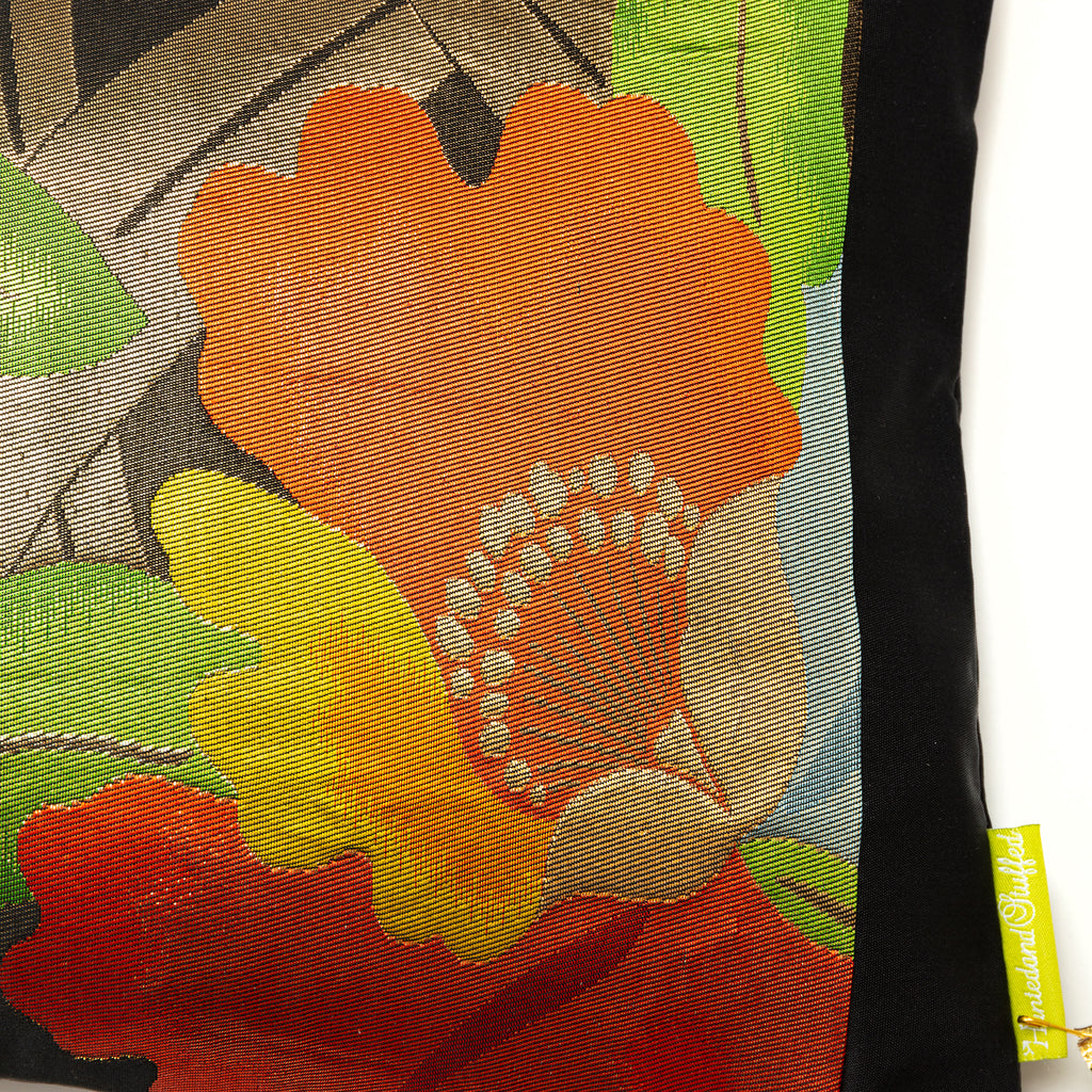 Close up of a black silk vintage obi cushion with black border and a red camellia flower with gold stamen and green leaves.