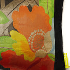 Close up of a black silk vintage obi cushion with black border and a red camellia flower with gold stamen and green leaves.